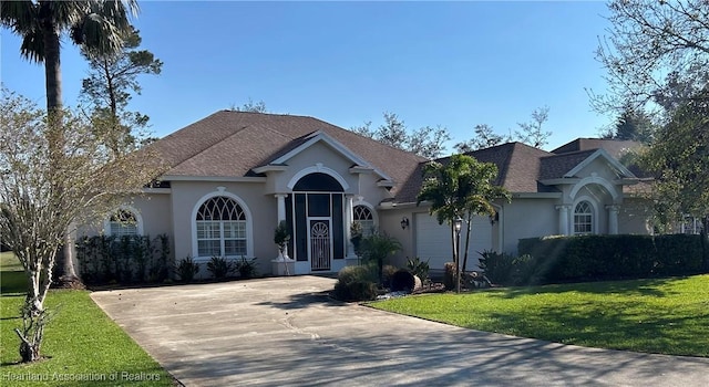 view of front of property with driveway, roof with shingles, an attached garage, a front lawn, and stucco siding