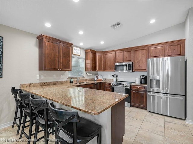 kitchen featuring sink, stainless steel appliances, a kitchen bar, vaulted ceiling, and kitchen peninsula