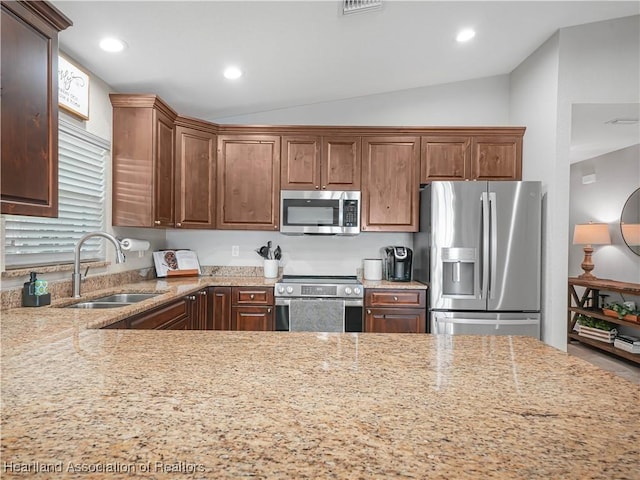 kitchen featuring vaulted ceiling, stainless steel appliances, a sink, and light stone countertops