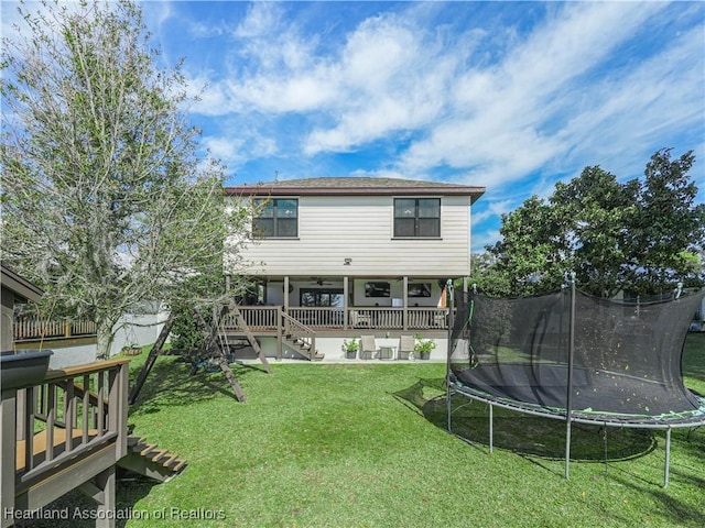 rear view of house with a trampoline, a lawn, stairway, and a deck