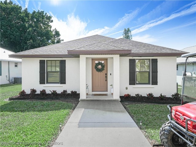 view of front of property featuring a shingled roof, a front lawn, cooling unit, and stucco siding