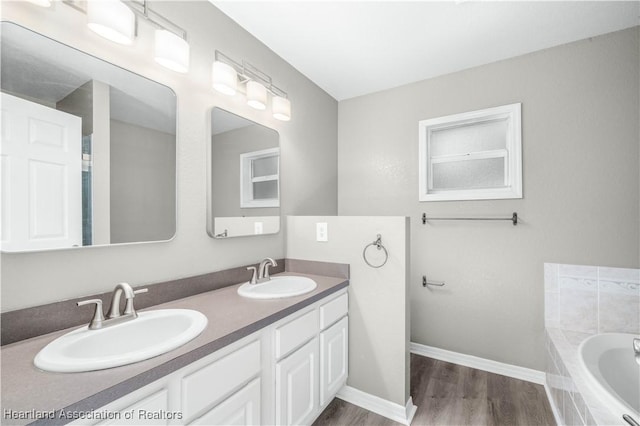 bathroom featuring a relaxing tiled tub, wood-type flooring, and vanity