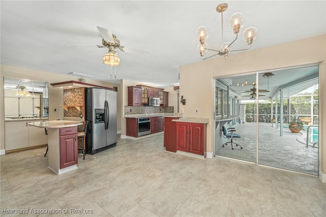 kitchen featuring a center island, stainless steel appliances, a kitchen bar, decorative backsplash, and ceiling fan with notable chandelier