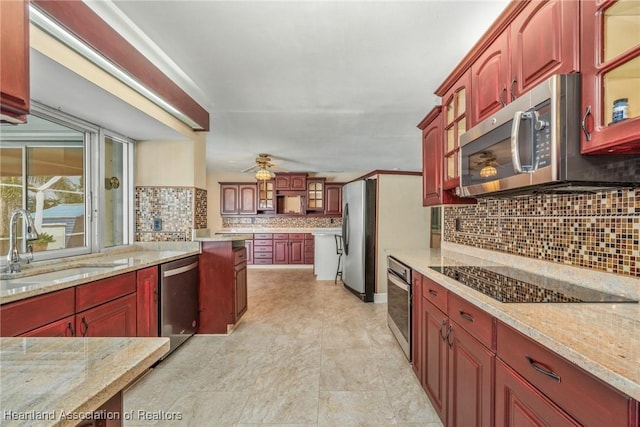 kitchen featuring backsplash, light stone counters, stainless steel appliances, ceiling fan, and sink