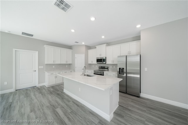 4737 Myrtle Dr, Sebring, FL 33872 - kitchen with appliances with stainless steel finishes, light wood-style floors, white cabinetry, an island with sink, and backsplash