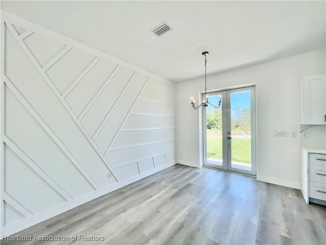 unfurnished dining area featuring a chandelier, french doors, and light wood-type flooring