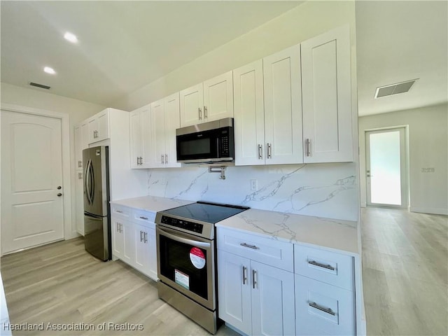 kitchen with light stone countertops, white cabinets, stainless steel appliances, light hardwood / wood-style floors, and backsplash