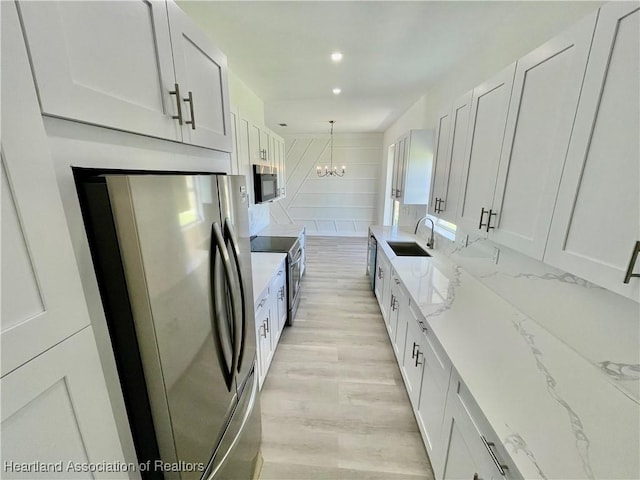 kitchen featuring white cabinetry, stainless steel appliances, hanging light fixtures, light stone countertops, and sink