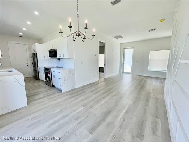 kitchen with an inviting chandelier, appliances with stainless steel finishes, white cabinets, and light stone countertops