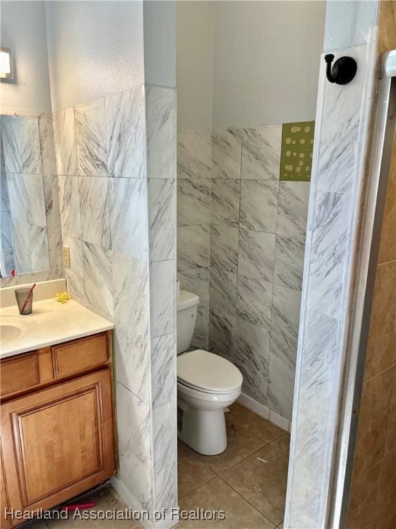 bathroom featuring tile patterned floors, vanity, toilet, and tile walls