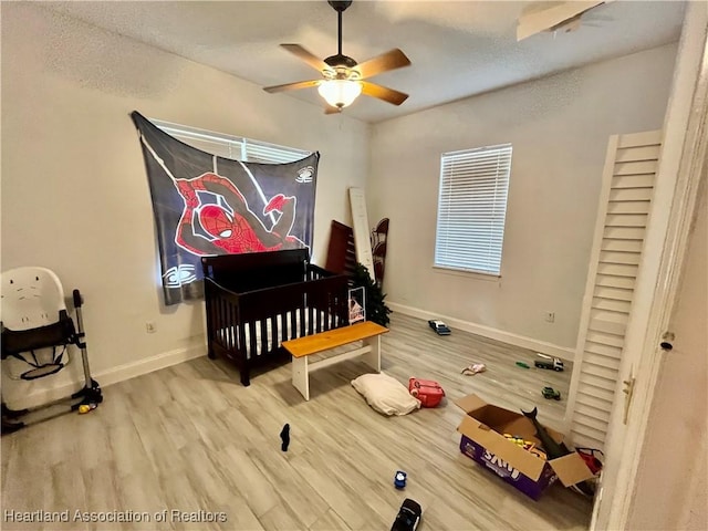 bedroom featuring ceiling fan, hardwood / wood-style floors, a nursery area, and a textured ceiling