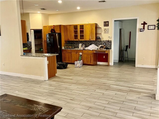 kitchen with light stone countertops, tasteful backsplash, refrigerator with ice dispenser, kitchen peninsula, and light wood-type flooring