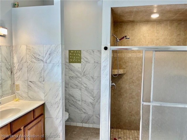 bathroom with tile patterned flooring, toilet, a shower with door, vanity, and tile walls