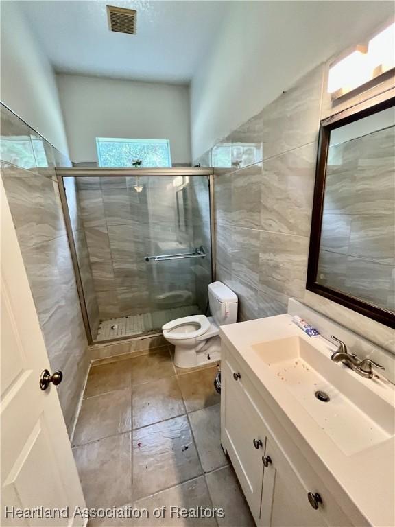 bathroom featuring vanity, toilet, walk in shower, and tile walls