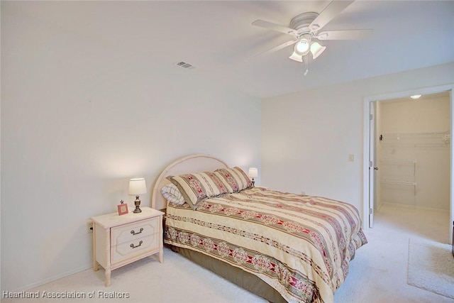 bedroom with a walk in closet, light colored carpet, a closet, and ceiling fan