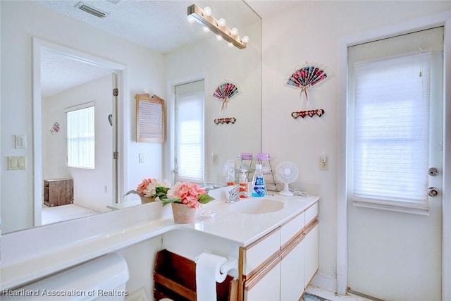 bathroom with plenty of natural light, toilet, a textured ceiling, and vanity