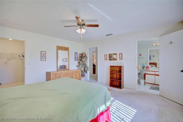 bedroom with light carpet, a walk in closet, a textured ceiling, ceiling fan, and a closet