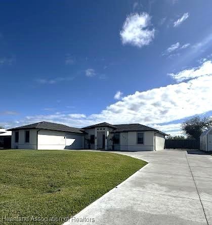 view of front facade featuring concrete driveway, a front lawn, and fence