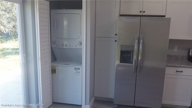 kitchen featuring stainless steel refrigerator with ice dispenser, white cabinetry, stacked washing maching and dryer, and light stone countertops