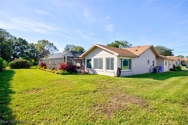 rear view of house with cooling unit, glass enclosure, a yard, and stucco siding