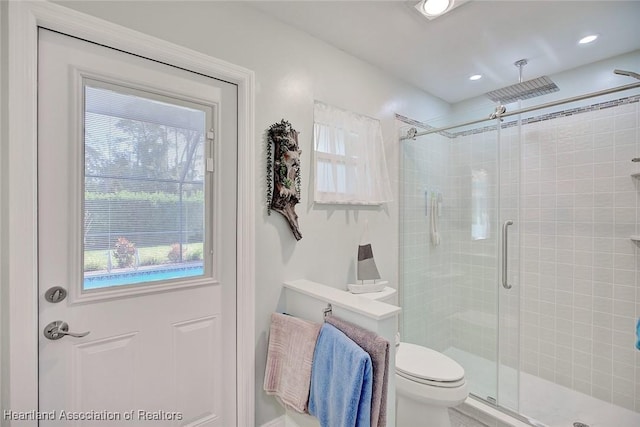 bathroom featuring toilet, a wealth of natural light, and a shower with shower door