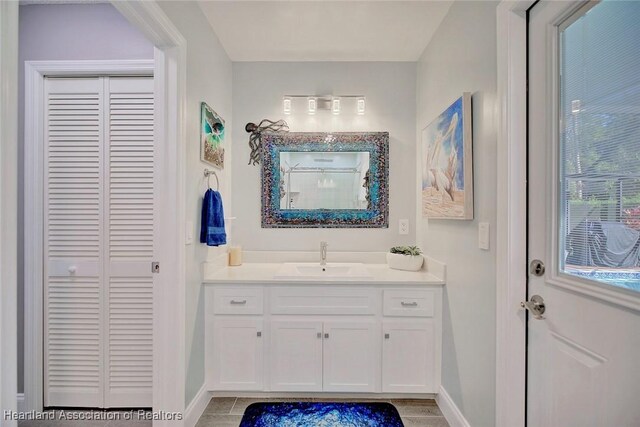 full bathroom with a closet, vanity, and baseboards