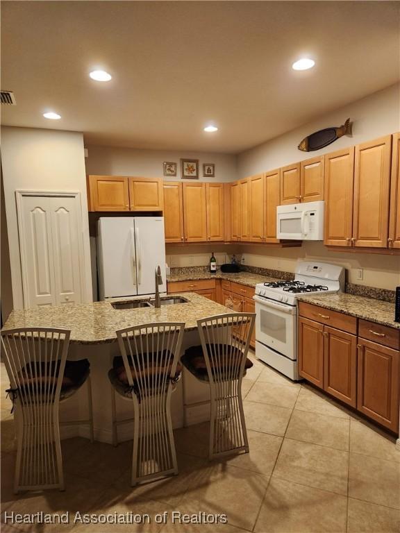 kitchen featuring white appliances, a kitchen island with sink, a breakfast bar area, and sink