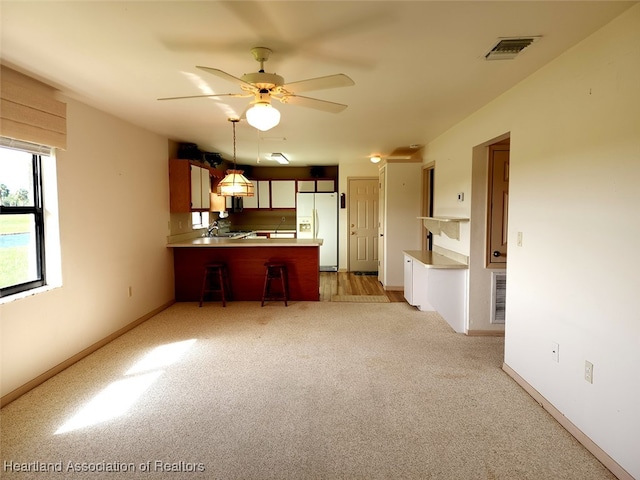 kitchen featuring light carpet, a kitchen bar, kitchen peninsula, ceiling fan, and white fridge with ice dispenser