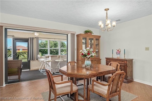 dining area featuring visible vents, an inviting chandelier, light wood-style floors, a textured ceiling, and baseboards