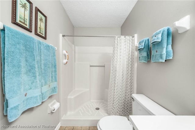 full bathroom featuring toilet, a stall shower, a textured ceiling, and vanity