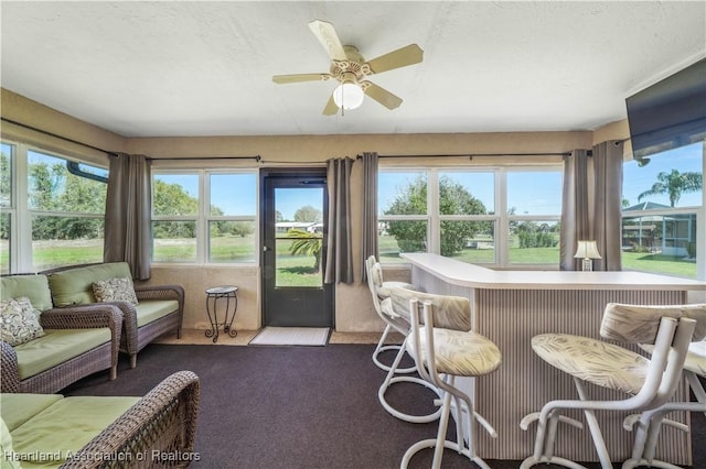 sunroom / solarium featuring ceiling fan and a bar