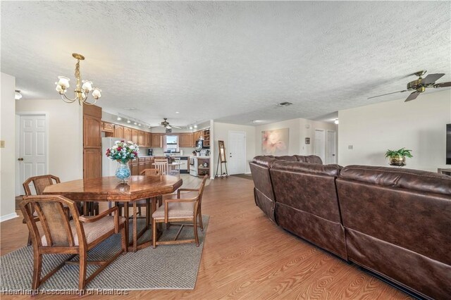 dining area featuring light wood-style flooring, a textured ceiling, and ceiling fan with notable chandelier