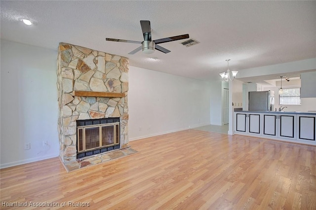 unfurnished living room featuring a fireplace, light hardwood / wood-style floors, a textured ceiling, and ceiling fan with notable chandelier