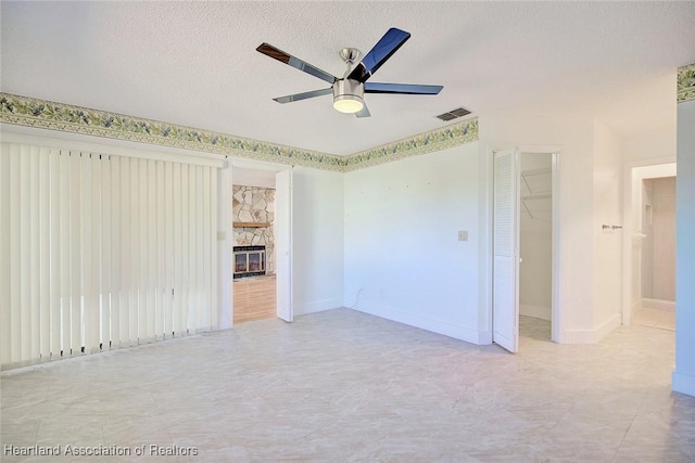 spare room with ceiling fan, a fireplace, and a textured ceiling