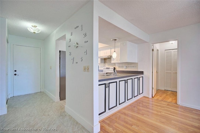 kitchen with backsplash, electric range, a textured ceiling, decorative light fixtures, and white cabinetry