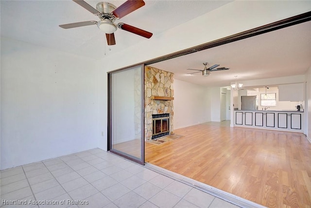 unfurnished living room featuring ceiling fan with notable chandelier, sink, light wood-type flooring, and a fireplace