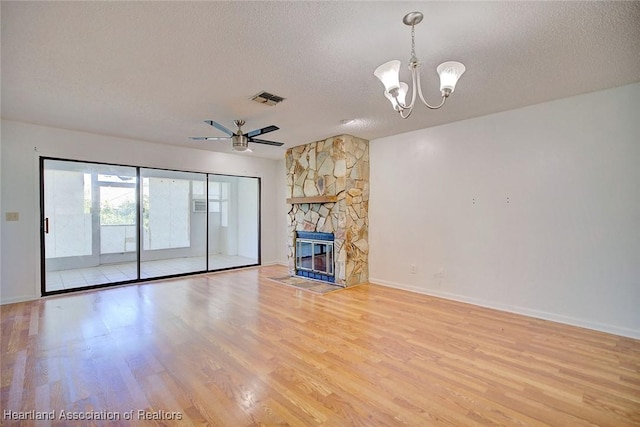 unfurnished living room with ceiling fan with notable chandelier, hardwood / wood-style floors, a textured ceiling, and a stone fireplace