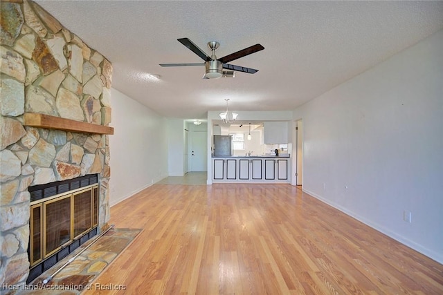 unfurnished living room featuring ceiling fan, a fireplace, a textured ceiling, and light hardwood / wood-style flooring