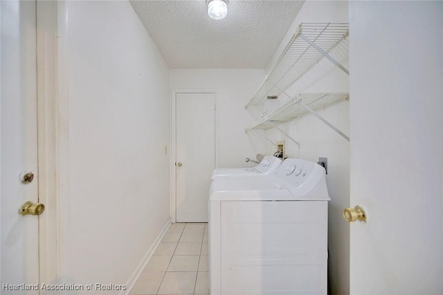 clothes washing area with washing machine and clothes dryer, light tile patterned flooring, and a textured ceiling