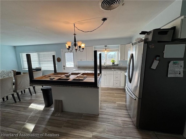 kitchen with sink, white cabinetry, a chandelier, hanging light fixtures, and stainless steel refrigerator