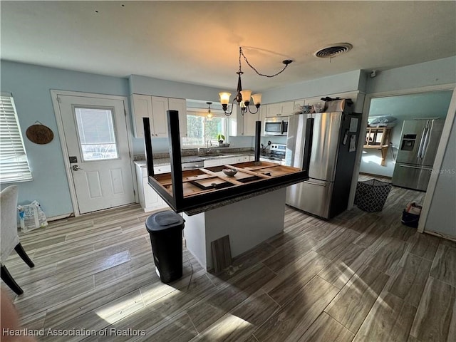 kitchen featuring sink, appliances with stainless steel finishes, white cabinetry, an inviting chandelier, and a center island