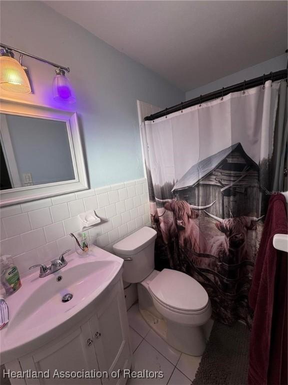 bathroom featuring toilet, tile walls, vanity, curtained shower, and tile patterned flooring