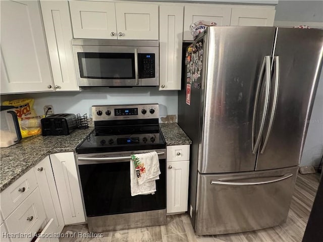 kitchen with white cabinetry, light wood-type flooring, dark stone countertops, and appliances with stainless steel finishes