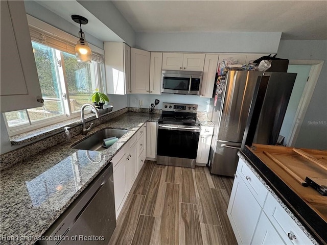 kitchen with sink, hanging light fixtures, dark stone countertops, appliances with stainless steel finishes, and white cabinets