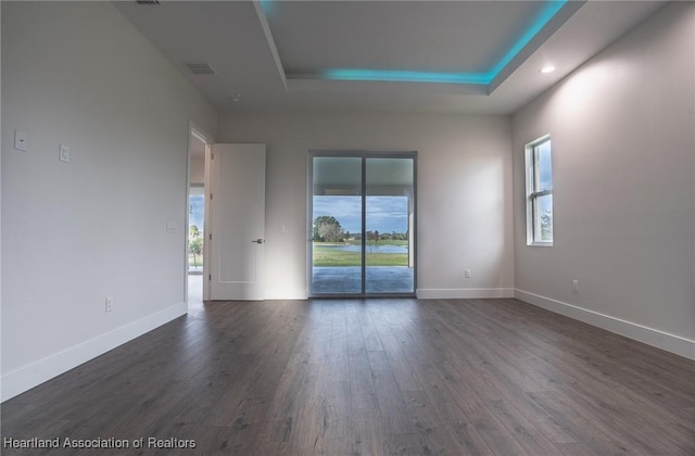 empty room with dark hardwood / wood-style flooring and a raised ceiling