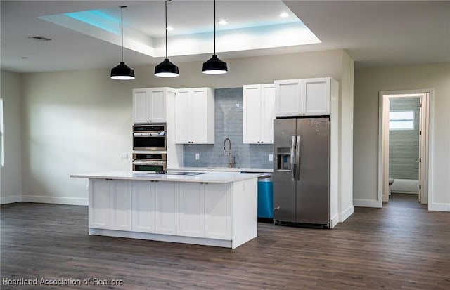 kitchen with pendant lighting, white cabinets, a raised ceiling, appliances with stainless steel finishes, and a kitchen island