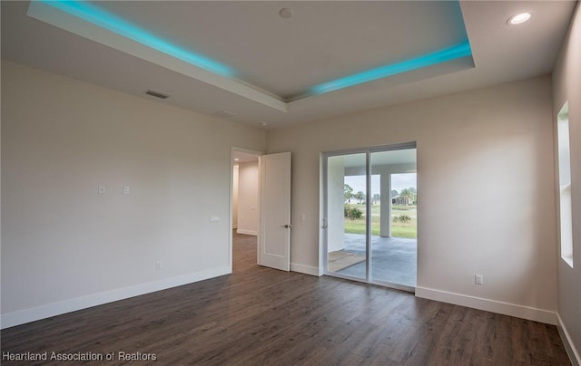 empty room with a tray ceiling and dark hardwood / wood-style floors