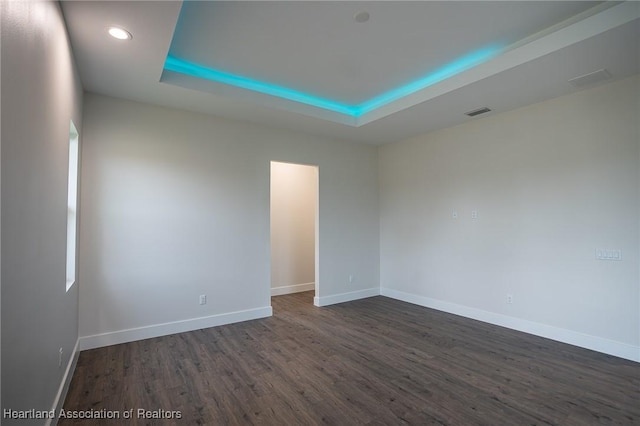 spare room with a raised ceiling and dark wood-type flooring