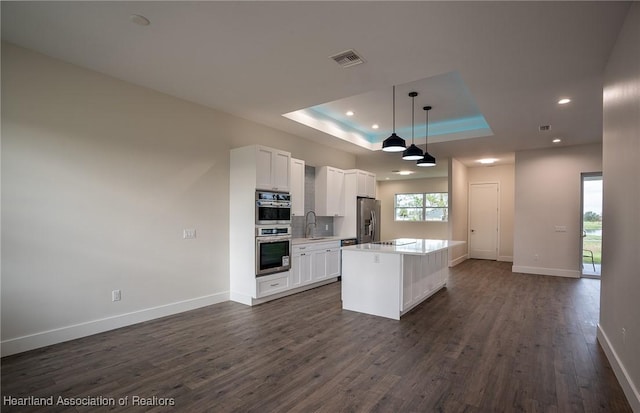 kitchen featuring white cabinets, a raised ceiling, sink, appliances with stainless steel finishes, and decorative light fixtures