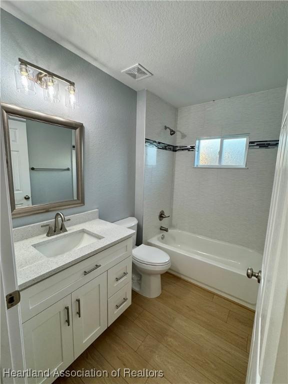 full bathroom featuring hardwood / wood-style floors, a textured ceiling, tiled shower / bath, vanity, and toilet